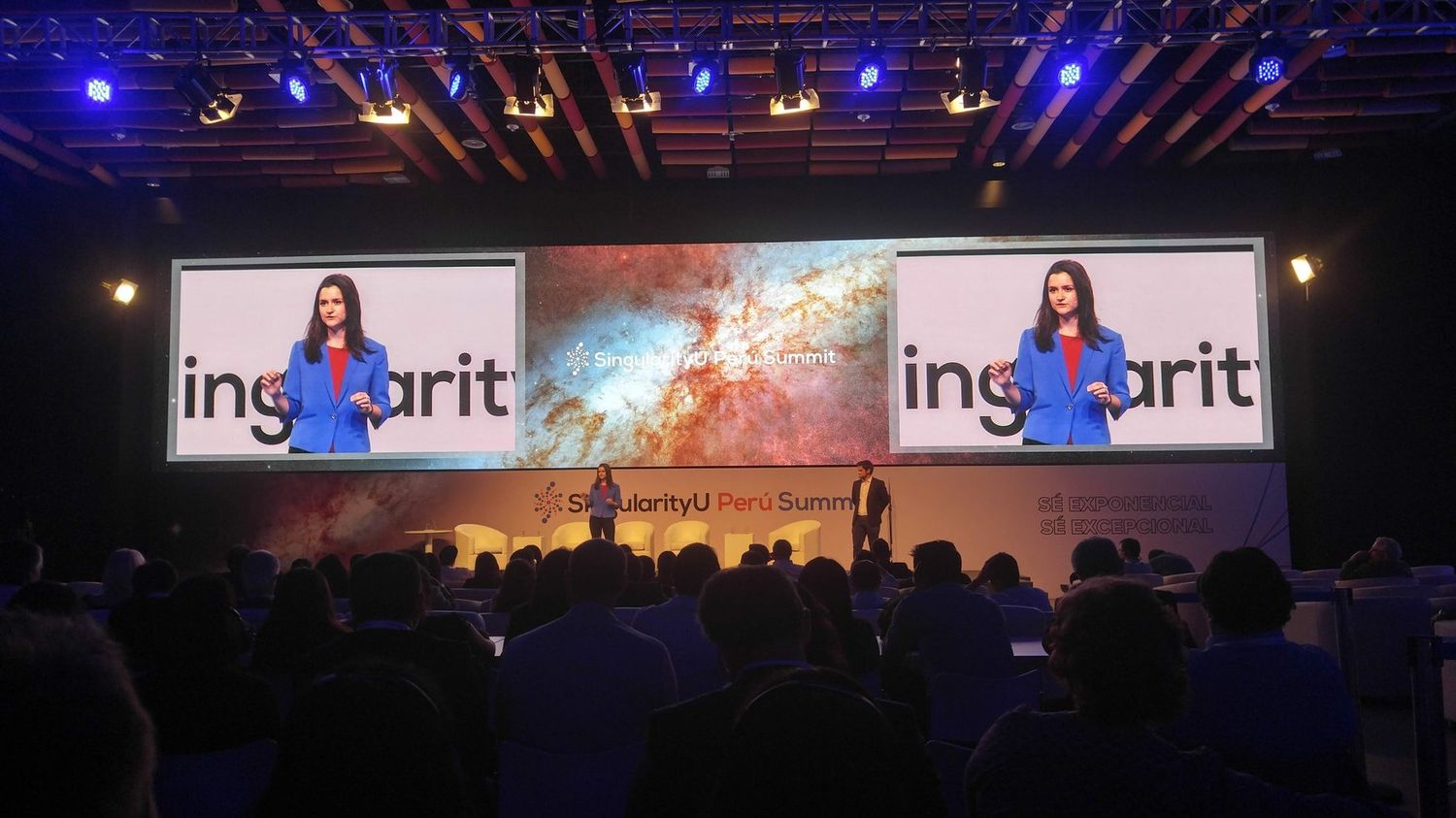 Pilar Dueñas on the main stage at the SingularityU Summit, her image on two large screens above a full auditorium